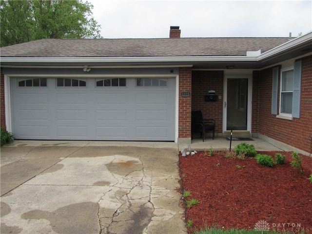 view of front of home with a chimney, a garage, brick siding, concrete driveway, and a shingled roof