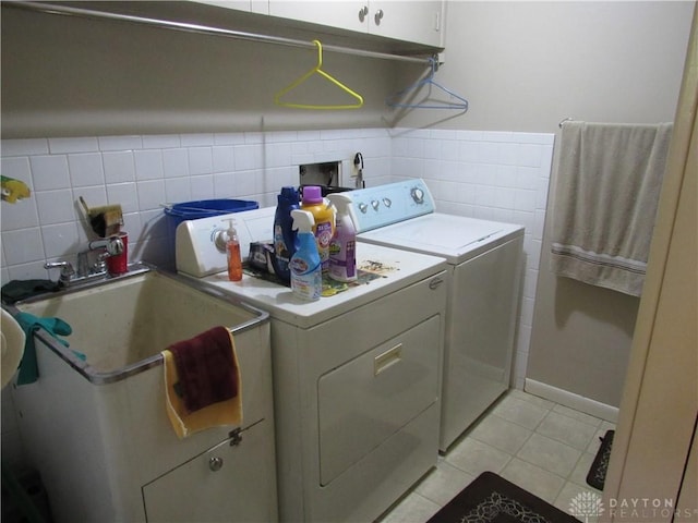 washroom with cabinet space, light tile patterned flooring, a sink, tile walls, and washing machine and dryer