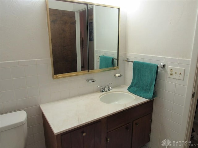 bathroom with toilet, tile walls, a wainscoted wall, and vanity