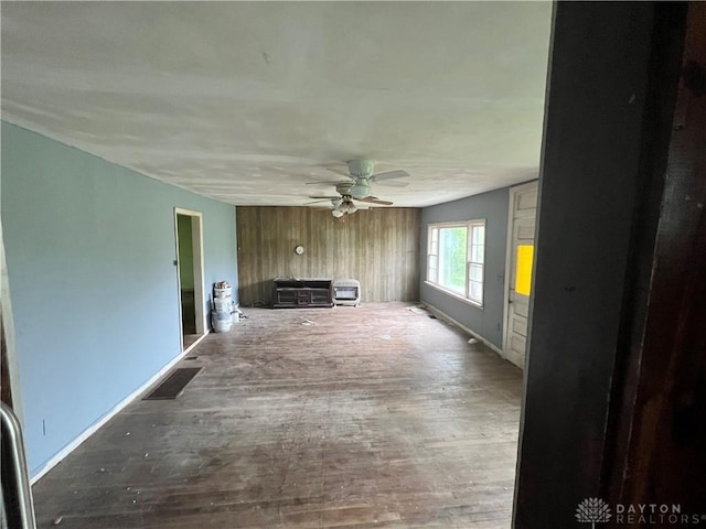 unfurnished living room featuring baseboards, visible vents, ceiling fan, wooden walls, and wood finished floors