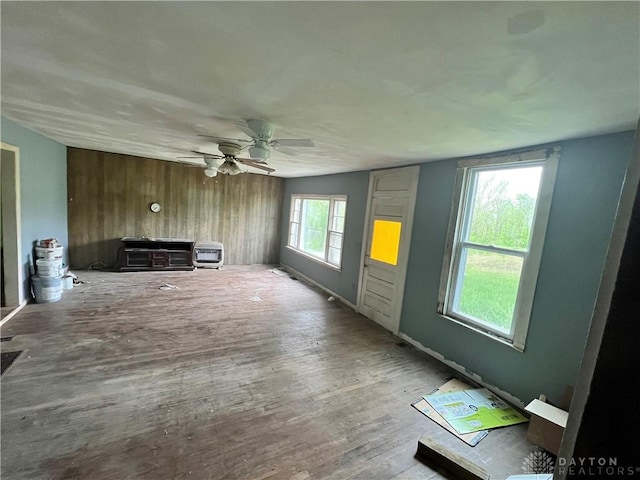 unfurnished living room with wood walls, ceiling fan, and wood finished floors