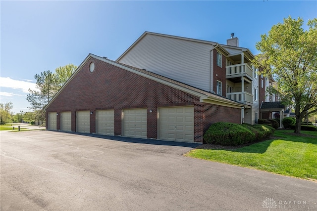 view of property exterior featuring a chimney, community garages, brick siding, and a lawn