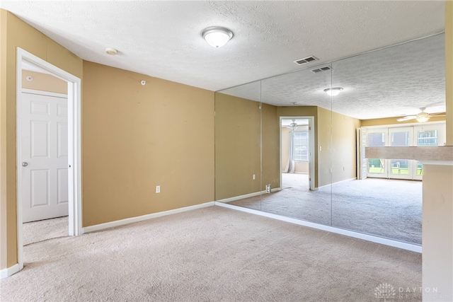 unfurnished room featuring carpet, a ceiling fan, a textured ceiling, visible vents, and baseboards