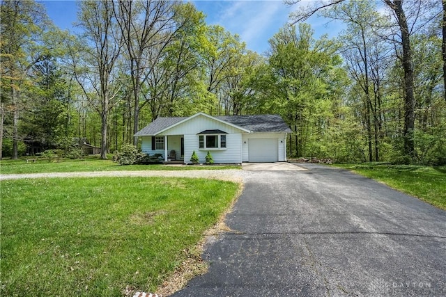 view of front of house featuring covered porch, aphalt driveway, an attached garage, a view of trees, and a front lawn