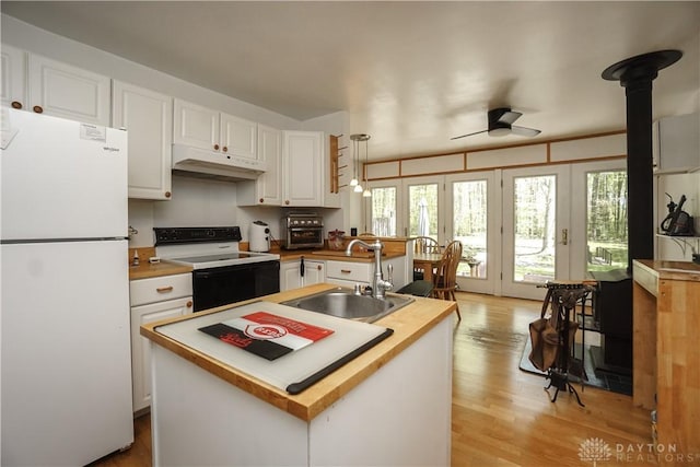 kitchen with a sink, freestanding refrigerator, under cabinet range hood, white cabinets, and range with electric cooktop
