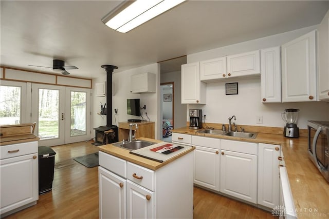 kitchen with a wood stove, butcher block countertops, a sink, and white cabinets