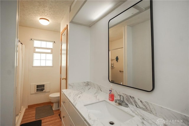 bathroom with toilet, wood finished floors, vanity, a textured ceiling, and heating unit