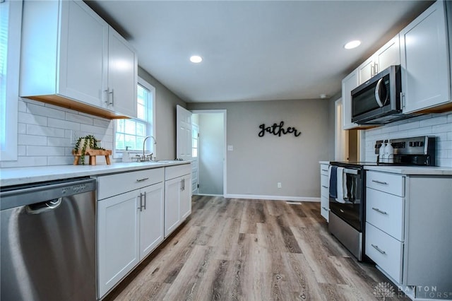 2004 N Reardon Dr, Dayton, OH 45420 - kitchen with a sink, tasteful backsplash, light wood-type flooring, white cabinetry, and appliances with stainless steel finishes