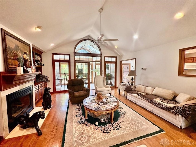 living area featuring ceiling fan, light wood-style flooring, lofted ceiling, and a fireplace with flush hearth