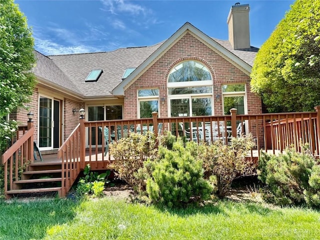 rear view of property with a chimney, a deck, roof with shingles, and brick siding