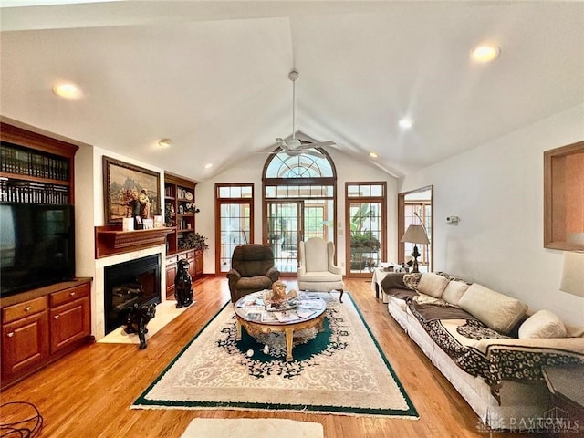 living room with vaulted ceiling, ceiling fan, a fireplace with flush hearth, and light wood-style floors