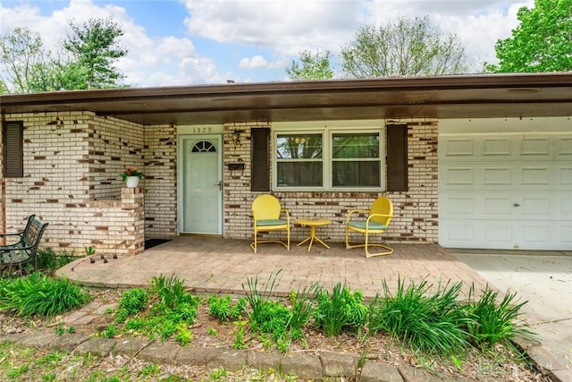 view of exterior entry featuring driveway, brick siding, covered porch, and an attached garage