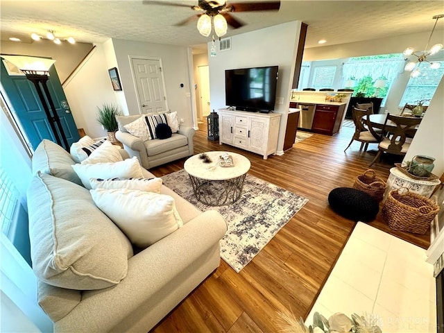 living room featuring dark wood-style flooring, ceiling fan with notable chandelier, and visible vents