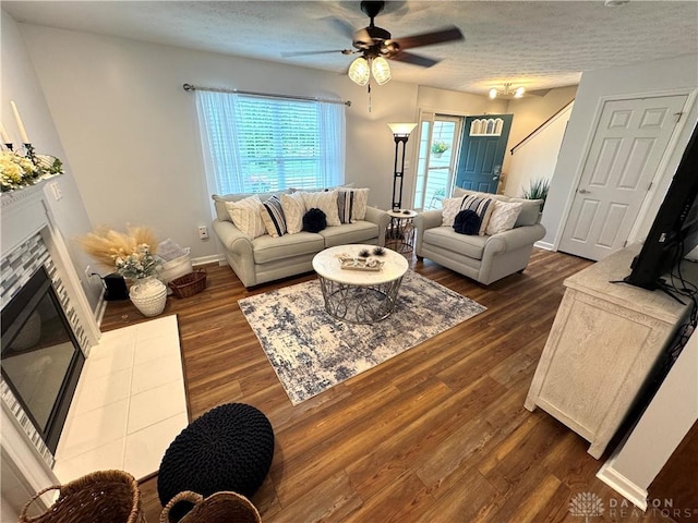 living area with ceiling fan, a textured ceiling, dark wood-style flooring, and a tiled fireplace