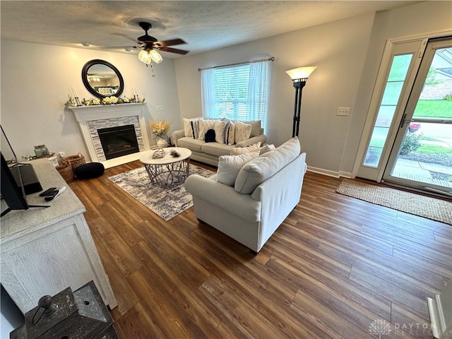 living area featuring dark wood-style flooring, a fireplace, a ceiling fan, and a healthy amount of sunlight