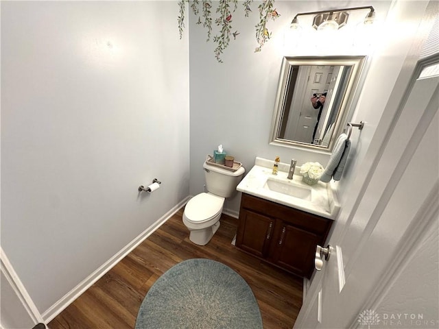 half bathroom with vanity, toilet, baseboards, and wood finished floors