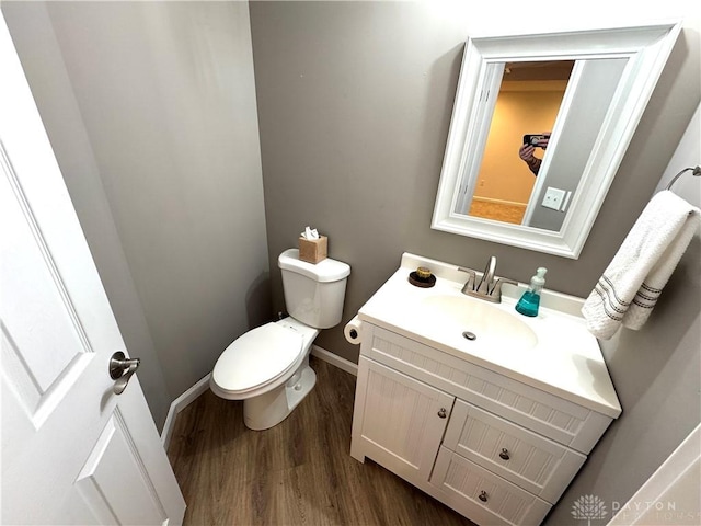 half bathroom featuring toilet, baseboards, vanity, and wood finished floors