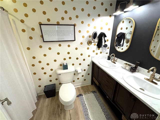 full bathroom with toilet, wallpapered walls, a sink, and wood finished floors
