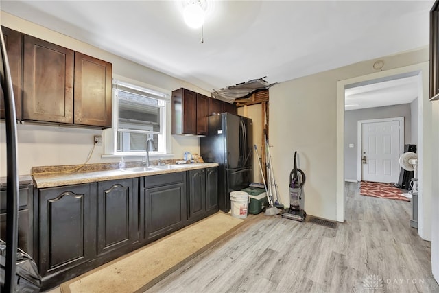 kitchen with freestanding refrigerator, a sink, dark brown cabinetry, light countertops, and light wood-type flooring