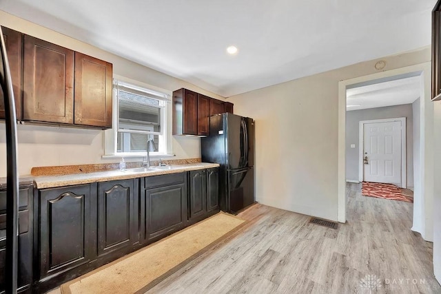 kitchen with freestanding refrigerator, visible vents, a sink, light countertops, and light wood-type flooring