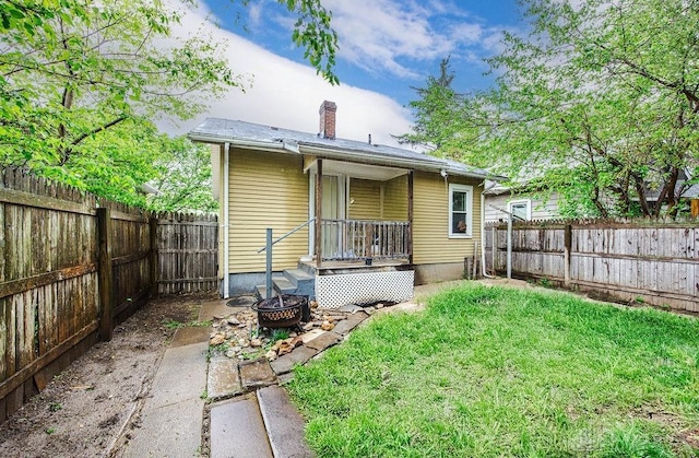 rear view of property featuring a fenced backyard, a fire pit, a chimney, and a yard