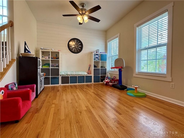 game room featuring a ceiling fan, baseboards, wooden walls, and light wood-type flooring