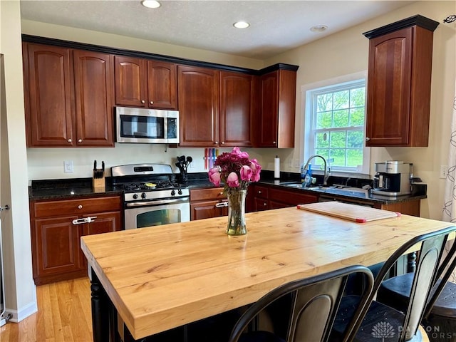 kitchen featuring light wood finished floors, a sink, wood counters, appliances with stainless steel finishes, and recessed lighting