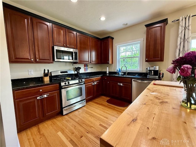 kitchen with light wood finished floors, wooden counters, a sink, appliances with stainless steel finishes, and recessed lighting
