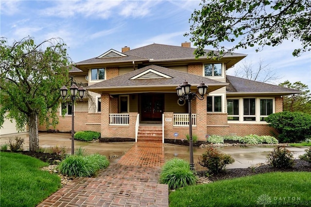 prairie-style home with a chimney, french doors, brick siding, covered porch, and a shingled roof