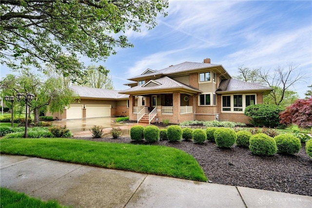 prairie-style house featuring a chimney, brick siding, covered porch, an attached garage, and concrete driveway
