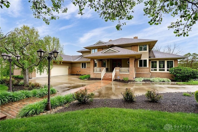prairie-style home with covered porch, concrete driveway, brick siding, and a garage