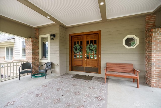 entrance to property with brick siding, french doors, and covered porch
