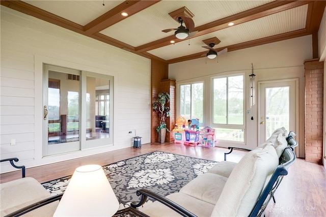 living area with visible vents, ceiling fan, wooden walls, wood finished floors, and beamed ceiling