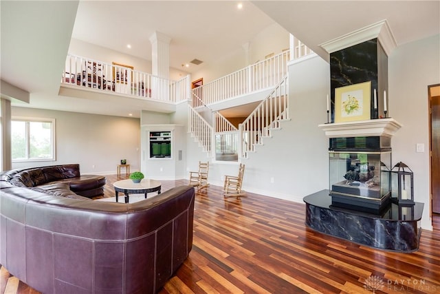 living room with a high end fireplace, wood finished floors, a towering ceiling, stairway, and baseboards