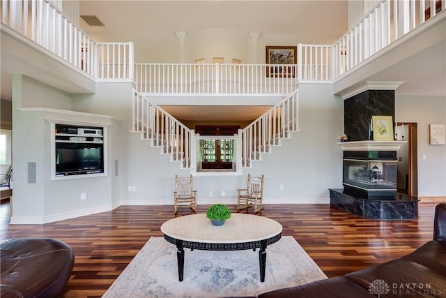 living area featuring stairway, a fireplace, a towering ceiling, and wood finished floors