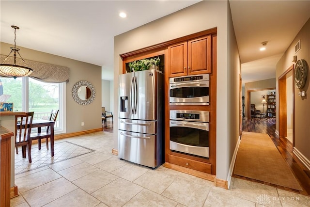 kitchen featuring hanging light fixtures, stainless steel appliances, brown cabinetry, visible vents, and baseboards