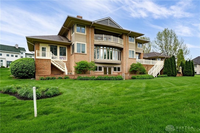 back of property featuring a chimney, a lawn, a balcony, brick siding, and stairs