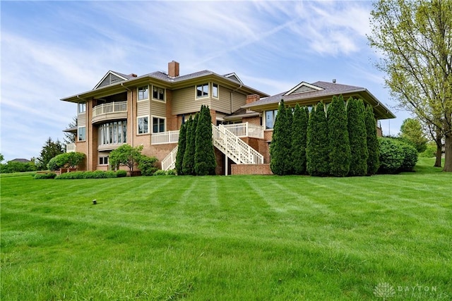 rear view of property with stairs, a chimney, and a lawn