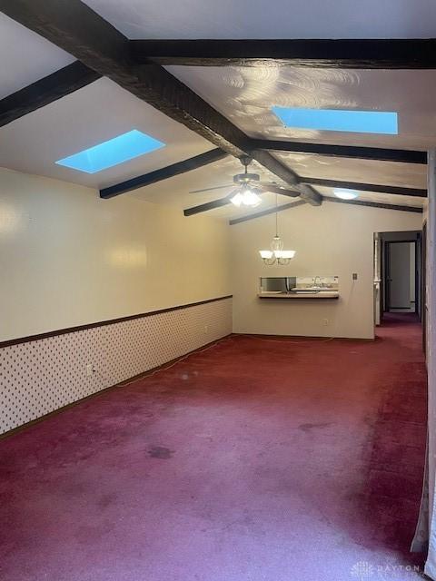 carpeted empty room featuring lofted ceiling with skylight and ceiling fan with notable chandelier