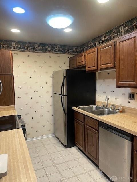 kitchen featuring a sink, light floors, dishwasher, baseboards, and wallpapered walls
