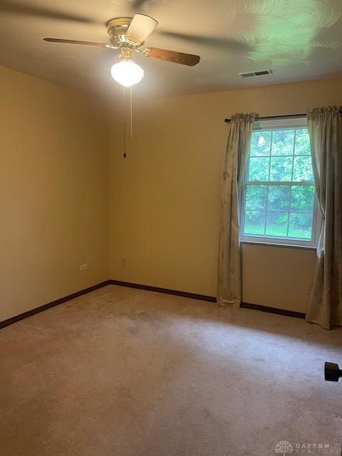 carpeted empty room with visible vents, baseboards, and a ceiling fan