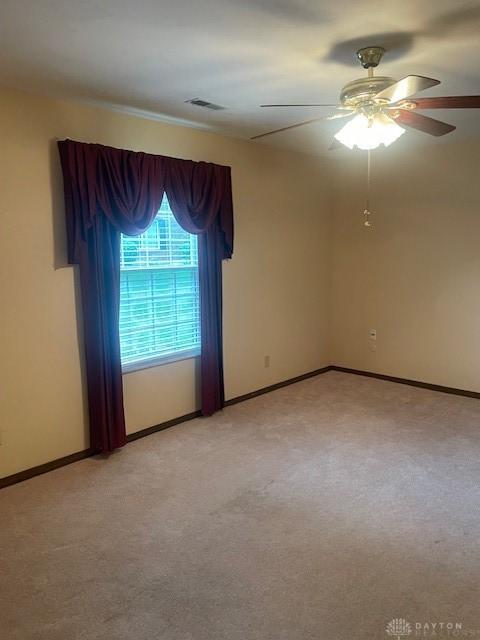 empty room featuring light colored carpet, baseboards, a ceiling fan, and visible vents