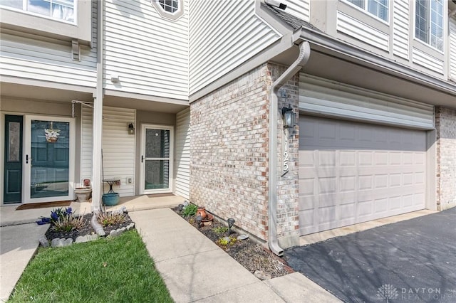 view of exterior entry with a garage and brick siding