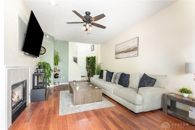 living room with a tile fireplace, ceiling fan, and wood finished floors