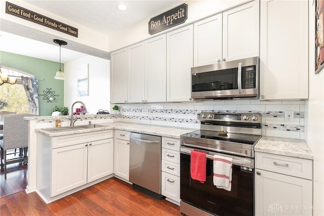 kitchen featuring stainless steel appliances, a peninsula, a sink, dark wood finished floors, and tasteful backsplash