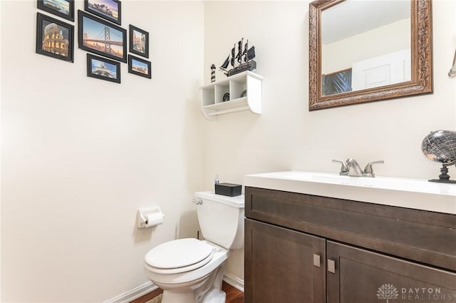 half bathroom with toilet, vanity, baseboards, and wood finished floors