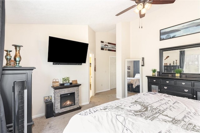 carpeted bedroom featuring baseboards, a stone fireplace, and a ceiling fan