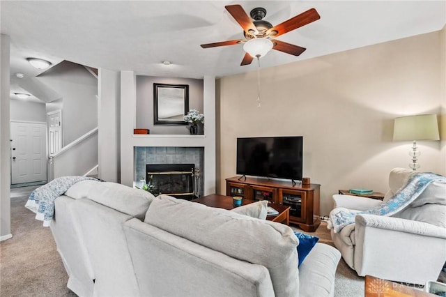 carpeted living area featuring ceiling fan, a fireplace, baseboards, and stairway