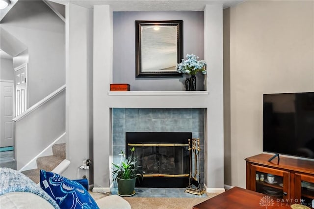 living room featuring stairway, a tiled fireplace, and baseboards