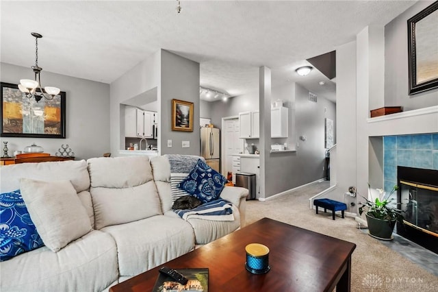 living area featuring a chandelier, light carpet, a tile fireplace, a textured ceiling, and baseboards